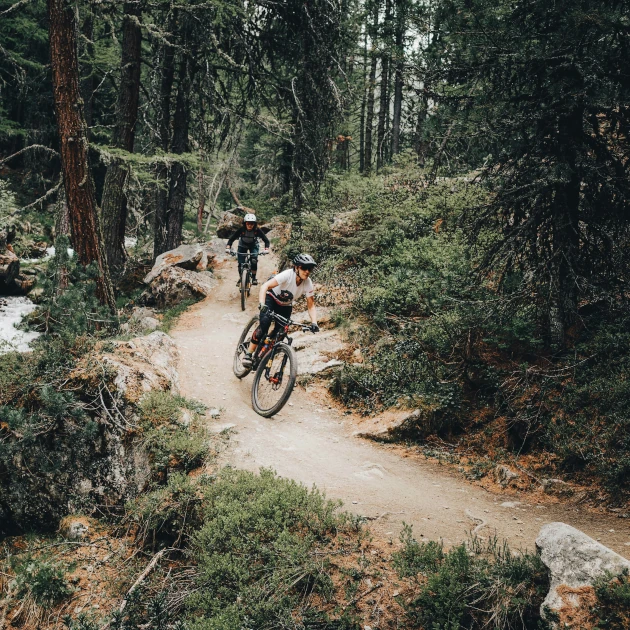 Two mountain bikers riding down a flow trail next to a river